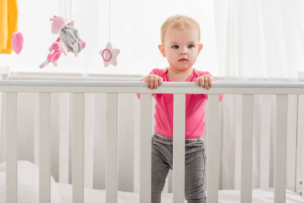 Adorable Niño Camisa Rosa Pie Cuna Mirando Hacia Otro Lado — Foto de stock gratis