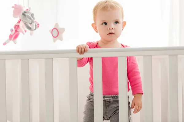 Adorable Child Pink Shirt Standing Crib Looking Away — Free Stock Photo