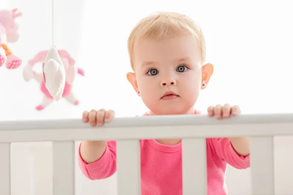 Çok Güzel Bebek Beşiğinde Ayakta Kameraya Bakarak Pembe Gömlekli — Stok fotoğraf