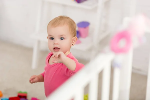 子供部屋のベッド近くに立っているピンクのシャツの愛らしい子供の選択と集中 — ストック写真