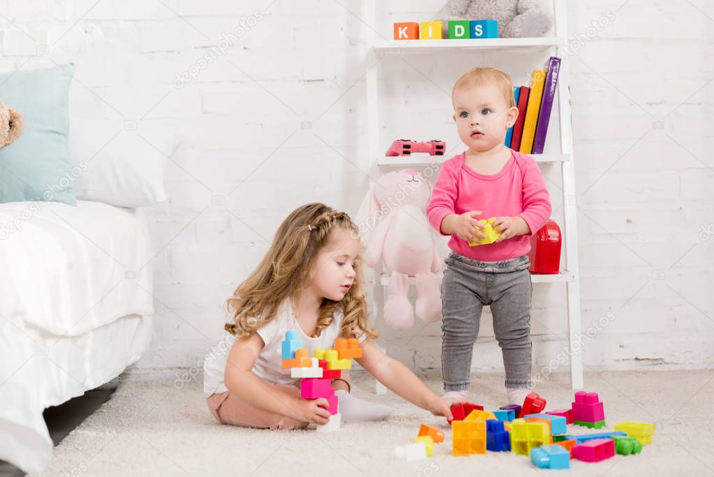 adorable sisters playing with constructor in children room