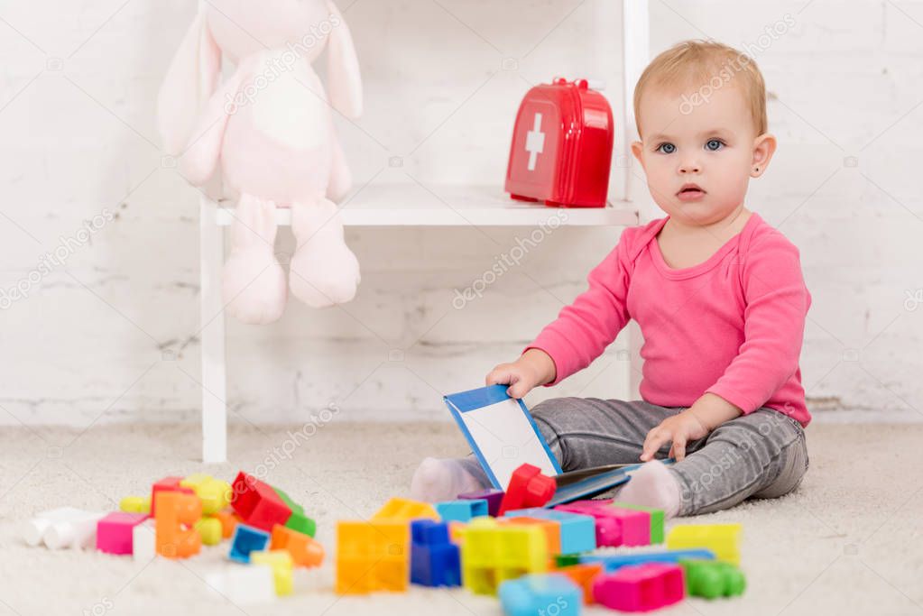 adorable kid sitting on carpet and holding book in children room