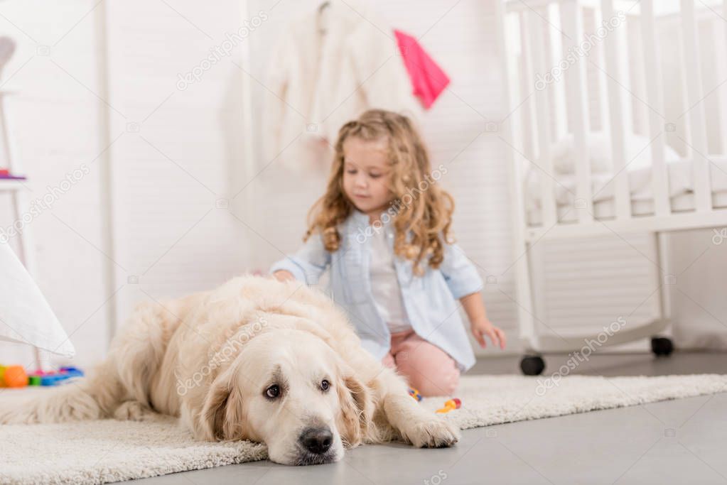 adorable kid sitting near golden retriever dog in children room