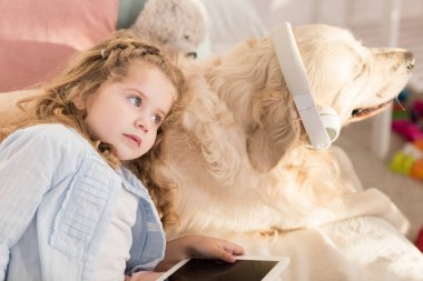 Tablet tutarak ve sevimli köpek çocuk odası yatakta yatan kulaklık ile eğilerek sevimli okul öncesi