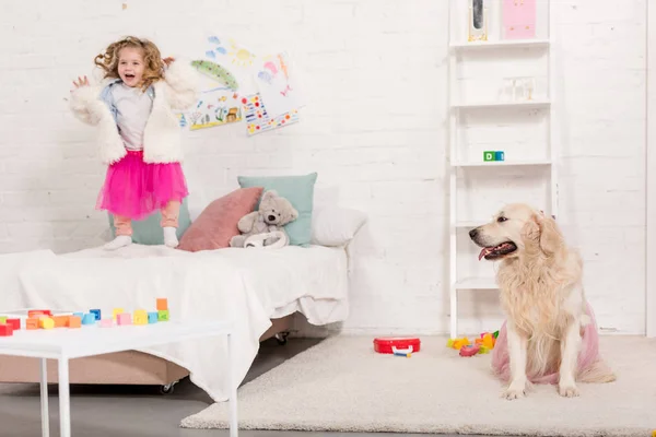 Excited Adorable Kid Jumping Bed Golden Retriever Sitting Carpet Pink — Stock Photo, Image