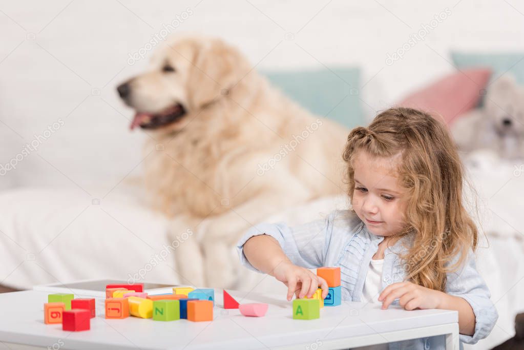 selective focus of adorable kid playing with educational cubes, golden retriever lying on bed in children room