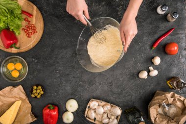 gri arka plan üzerinde Balon çırpıcı ve pizza malzemelerle un karıştırma kadının kısmi görünümü