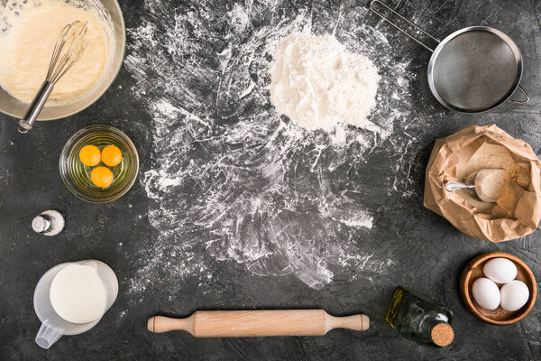 top view of dough, ingredients and cooking utensils on grey background