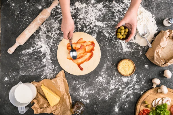 小麦粉と灰色の背景にピザを調理しながらソースを広める女性観をトリミング  — 無料ストックフォト