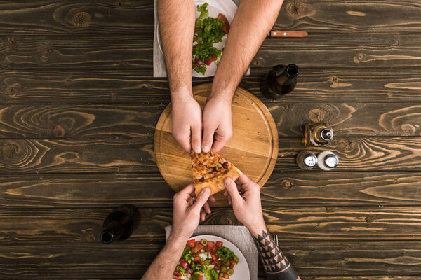 cropped view of men sharing slice of pizza during meal at wooden table
