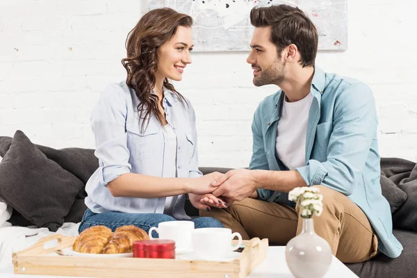 Pareja Sonriente Sentada Sofá Mirándose Unos Otros Tomándose Mano Mientras —  Fotos de Stock