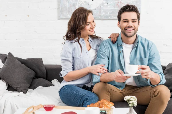 Mujer Sentada Sofá Mientras Sonríe Hombre Beber Café Durante Desayuno —  Fotos de Stock