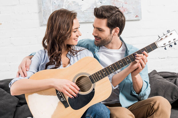 couple sitting on couch and playing acoustic guitar at home