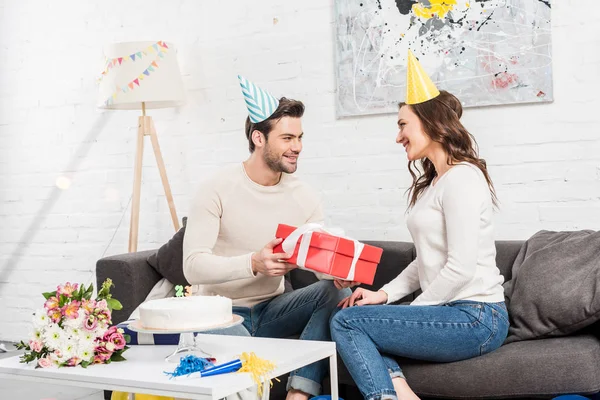 happy couple celebrating birthday and man presenting gift box to woman in living room