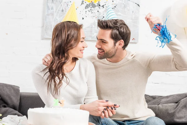 幸福的夫妇在党的帽子庆祝生日与蛋糕和党的号角在家里 — 图库照片