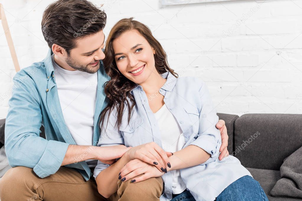happy couple sitting on couch and embracing at home 