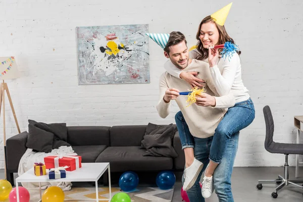 夫妇在党的号角和党的帽子庆祝生日 而男子给搭便车的女人在客厅 — 图库照片