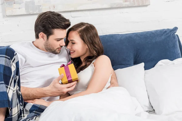 Lindo Casal Deitado Cama Abraçando Segurando Presente Aniversário Casa — Fotografia de Stock