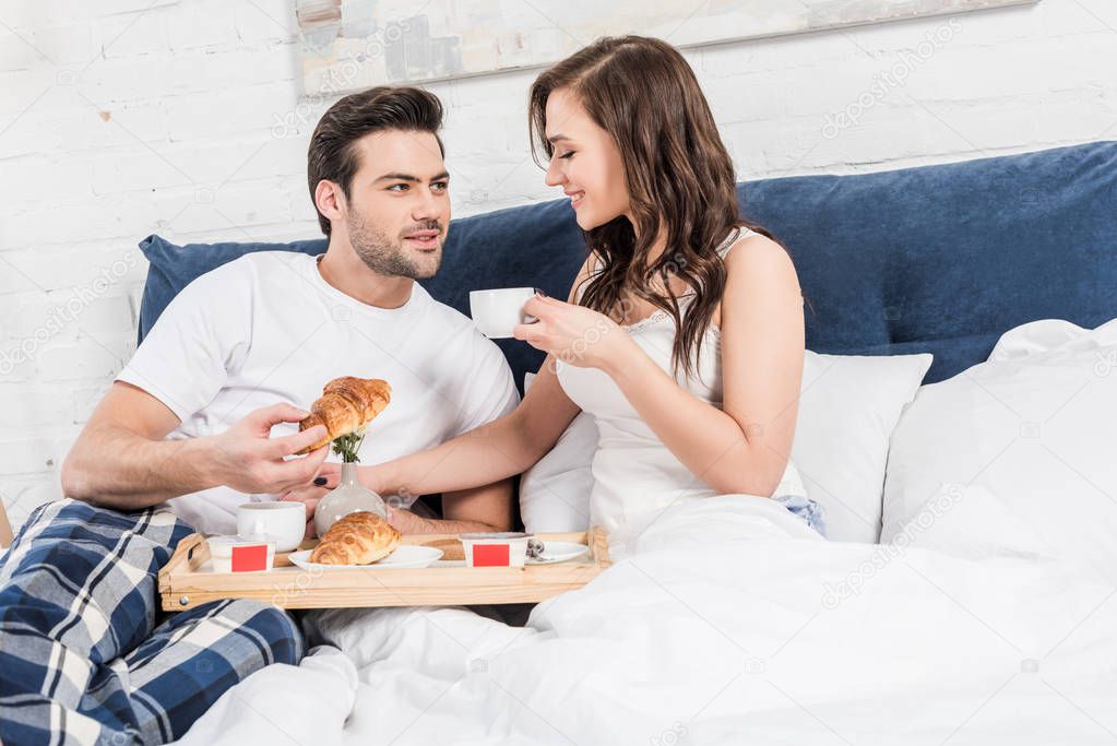 couple lying in bed and having breakfast in morning at home 