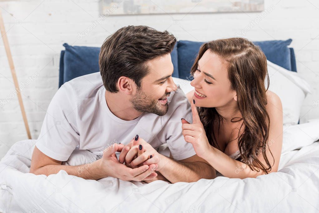 couple lying in bed while woman smiling and pointing with finger