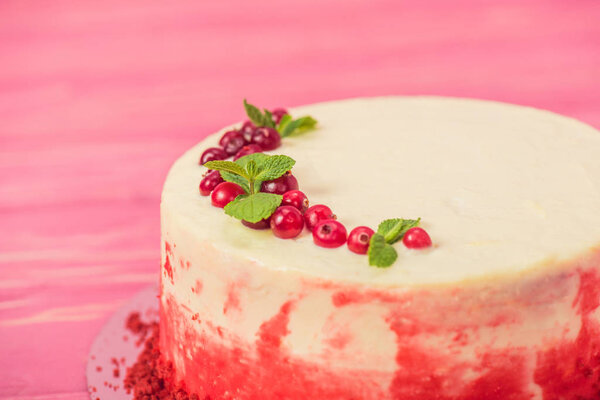 close up of white cake decorated with red currants and mint leaves 