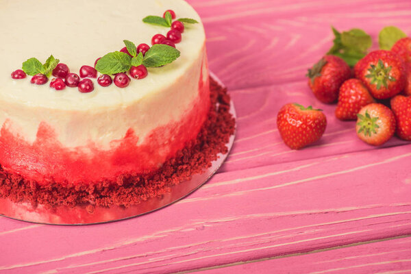 close up of white cake decorated with red currants and mint leaves near strawberries