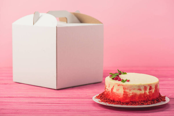 cake decorated with currants and mint leaves near white package isolated on pink