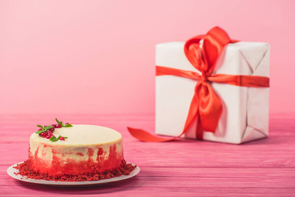 cake decorated with currants and mint leaves near gift box isolated on pink