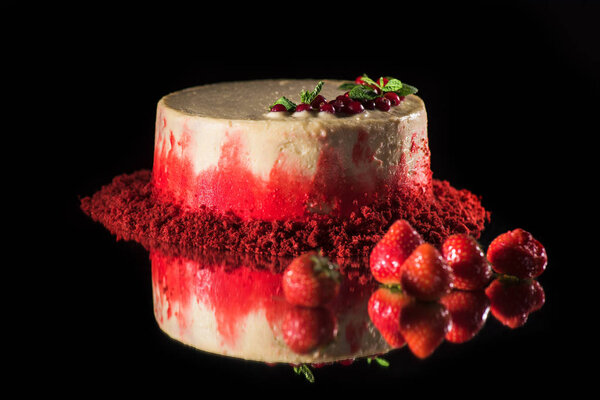 white cake decorated with red currants and mint leaves near strawberries isolated on black