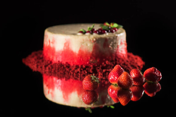 white cake decorated with red currants and mint leaves near strawberries isolated on black