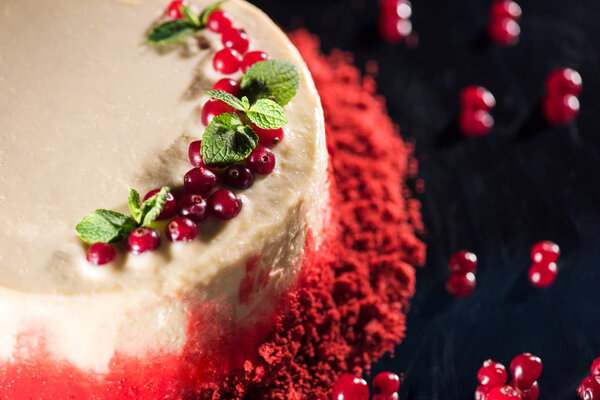 close up of white cake decorated with mint leaves near red currants isolated on black