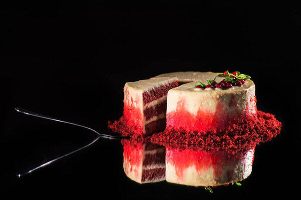 white cake decorated with mint leaves and red currants near spatula isolated on black