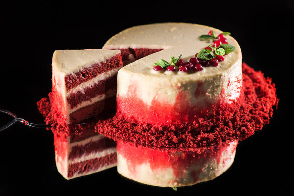 white cake decorated with mint leaves and red currants near spatula with piece of cake isolated on black