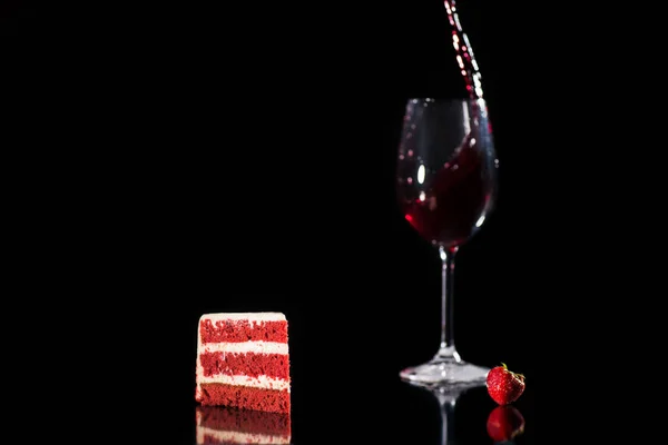 piece of red and white cake near glass of wine isolated on black