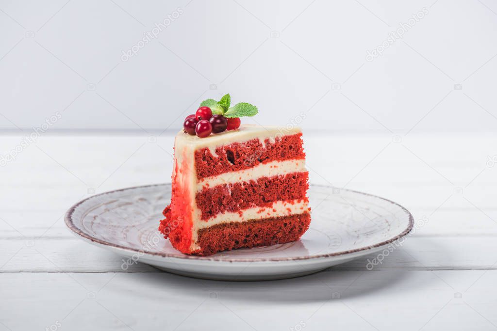 piece of red cake decorated with currants on saucer isolated on white 