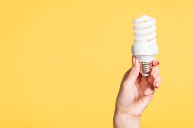 cropped view of female hand holding fluorescent lamp isolated on yellow, energy efficiency concept clipart