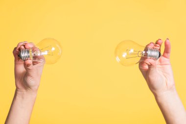 cropped view of female hands holding led lamps isolated on yellow, energy efficiency concept clipart