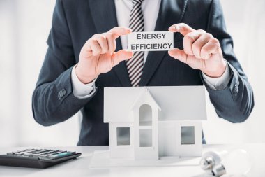 Beyaz arka planda, enerji verimliliği ev concept, kağıt kartı hesap makinesi ve lambaları yakın tutan işadamı kırpılmış görünümü