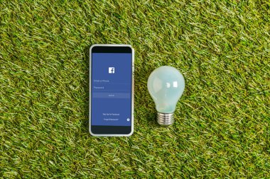 floresan lamba smartphone ile facebook app yakınındaki üstten görünüm ekranda yeşil çimen, enerji verimliliği kavramı 