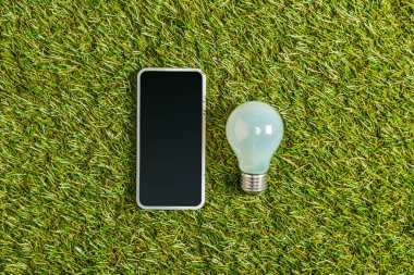 floresan lamba ile boş perde smartphone yakınındaki üstten görünüm yeşil çimen, enerji verimliliği kavramı üzerinde 