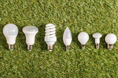 flat lay of fluorescent lamps on green grass, energy efficiency concept clipart