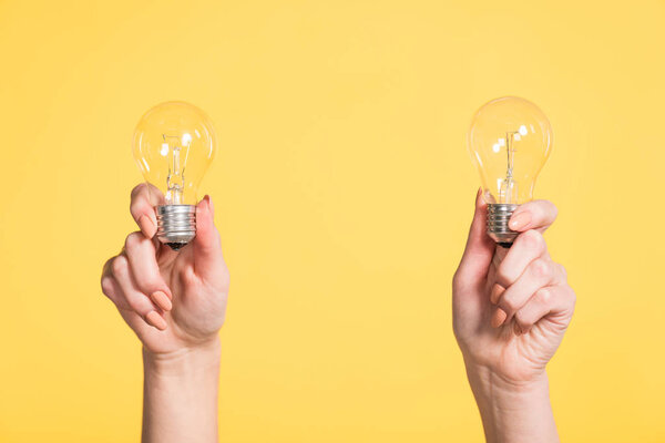 cropped view of woman holding led lamps in hands isolated on yellow, energy efficiency concept