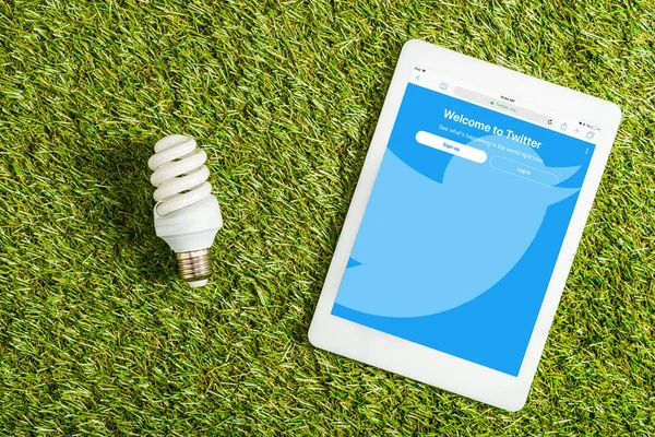 デジタル タブレットの Twitter アプリに近い蛍光灯の緑の草 エネルギー効率概念の画面上の表示トップ — ストック写真