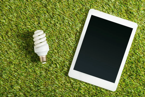 緑の草 エネルギー効率の概念に空白の画面を持つデジタル タブレットに近い蛍光ランプのトップ ビュー — ストック写真