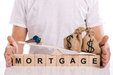 cropped view of man holding scales with moneybags and keys on cubes with mortgage lettering isolated on white clipart