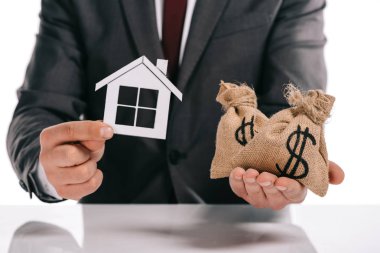 cropped view of mortgage broker holding paper house and moneybags isolated on white clipart