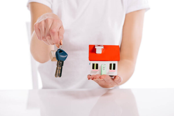 cropped view of woman holding house model and keys isolated on white, mortgage concept