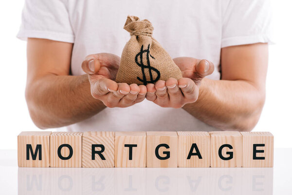 partial view of man holding moneybag near cubes with mortgage lettering isolated on white