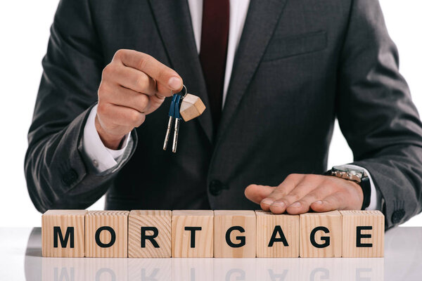 cropped view of businessman holding keys near wooden cubes with mortgage lettering isolated on white