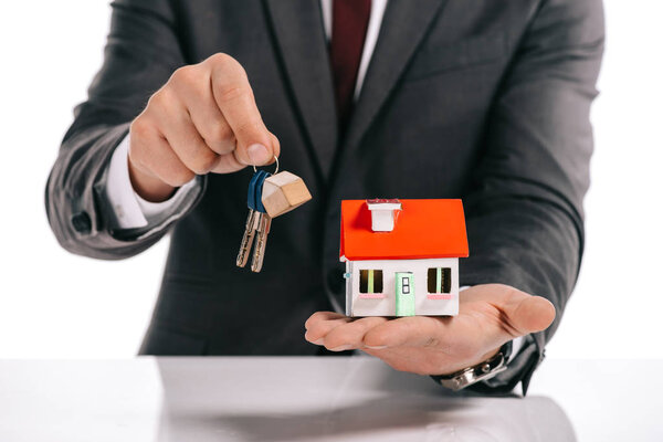 cropped view of mortgage broker holding house model and keys isolated on white